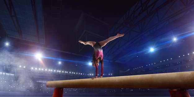 Gimnasta femenina haciendo un truco complicado en la barra de equilibrio de gimnasia en un campo profesional