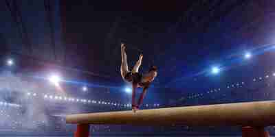 Foto gratuita gimnasta femenina haciendo un truco complicado en la barra de equilibrio de gimnasia en un campo profesional