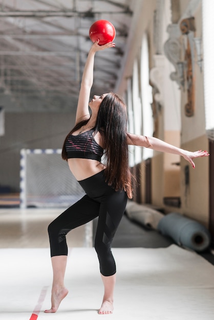 Gimnasta joven haciendo rutina con bola roja