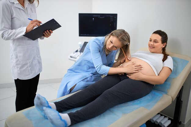 Ginecólogo de sexo femenino que controla la barriga de la mujer embarazada