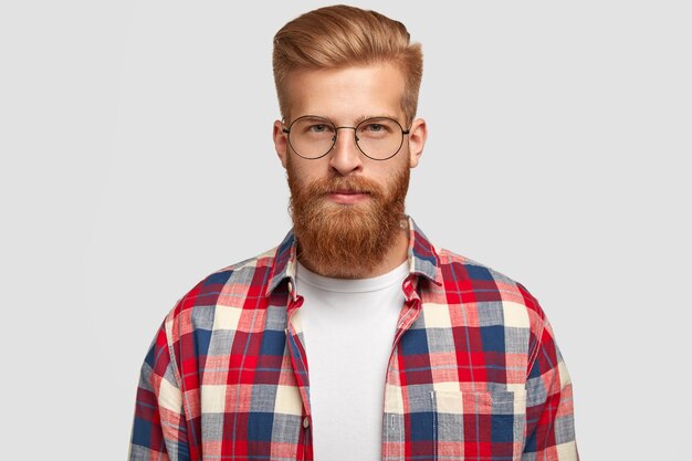 Ginger man hipster en gafas y camisa a cuadros, se ve serio con expresión facial segura, recibe la información necesaria