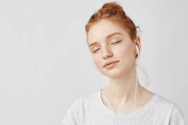Ginger mujer escuchando música en auriculares con los ojos cerrados.
