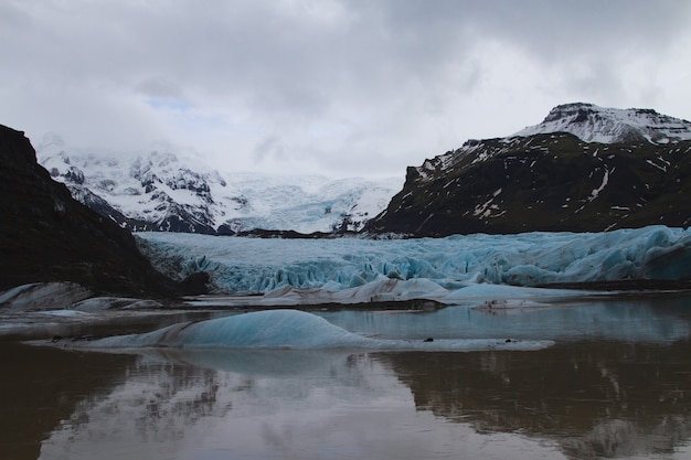 Glaciar rodeado de colinas cubiertas de nieve y reflejándose en el agua en Islandia