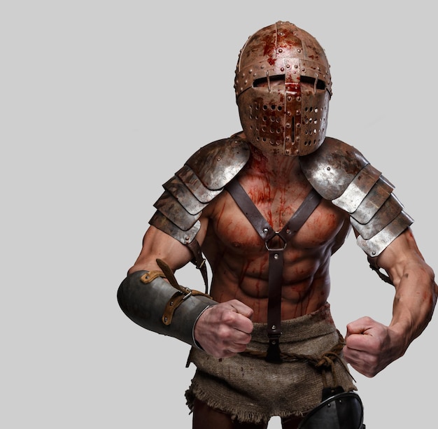 Gladiator en casco con cuerpo musculoso muestra su fuerza. Aislado en gris.