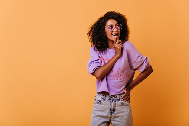 Glamorosa chica de pelo negro posando con placer en naranja. Modelo femenino optimista sonriendo.