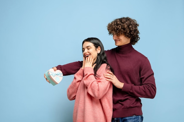 Globo de corazón, abrazando. Hermosa pareja de enamorados sobre fondo azul de estudio. Concepto de San Valentín, el amor, la relación y las emociones humanas. Copyspace. El hombre y la mujer se ven felices juntos.