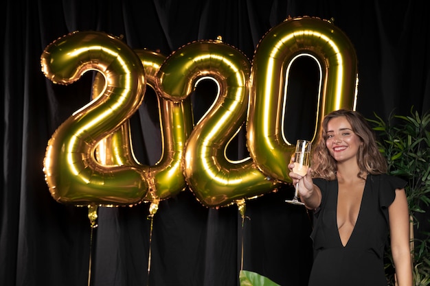 Globos dorados de año nuevo 2020 y linda chica sosteniendo una copa de champán