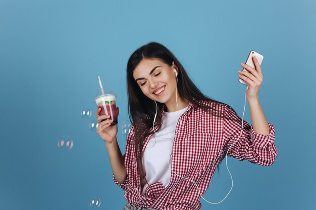 Globos de jabón vuelan alrededor de una niña feliz bebiendo batido de leche y bailando con los auriculares