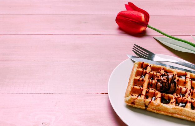 Gofre belga con tulipán rojo en mesa