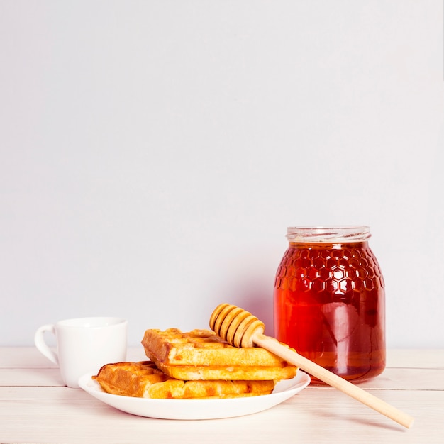Gofres deliciosos; tarro de miel y café para el desayuno en la mesa de madera