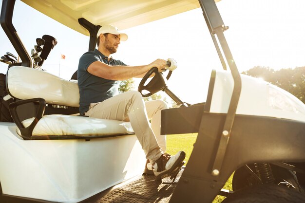 Golfista masculino conduciendo un carro con palos de golf