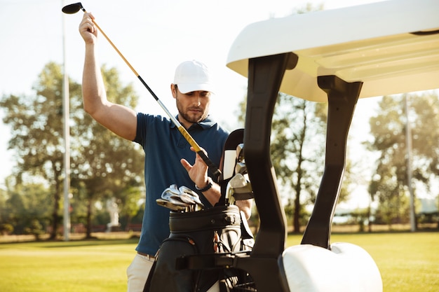 Golfista masculino guapo tomando palos de una bolsa en un carrito de golf