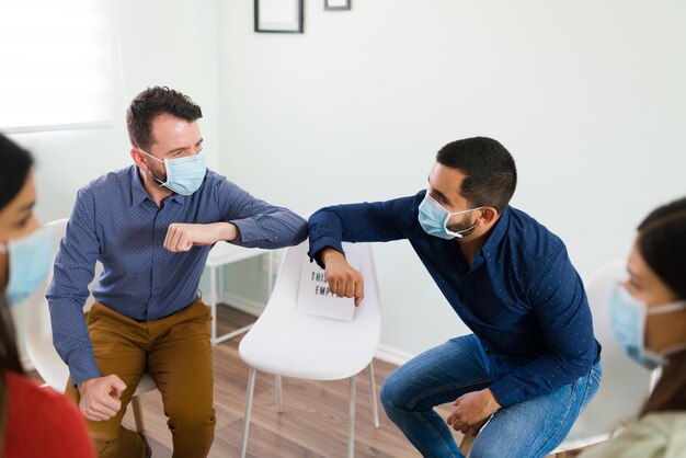 Golpe de codo. Dos jóvenes con mascarillas saludan antes de comenzar su reunión de alcohólicos anónimos