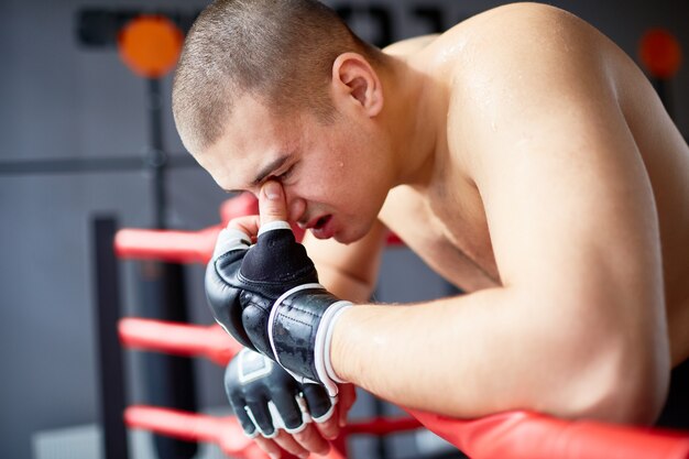 Golpeado boxeador apoyado en la baranda del anillo