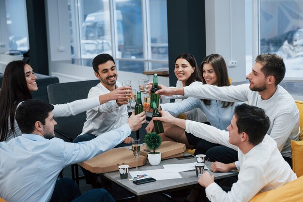 Golpeando botellas y vasos. Celebrando el trato exitoso. Jóvenes oficinistas sentados cerca de la mesa con alcohol