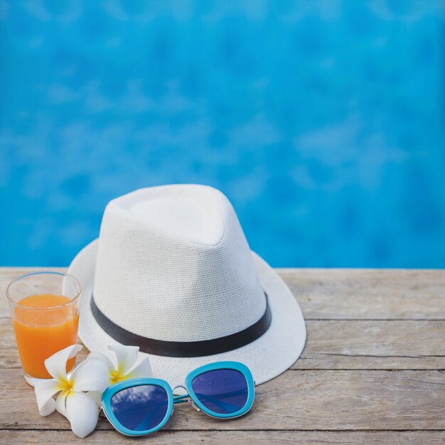 Gorro, gafas de sol y bebida con piscina de fondo