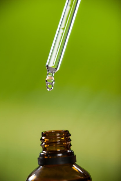 Gota de aceite que gotea de la pipeta en una botella de aceite esencial