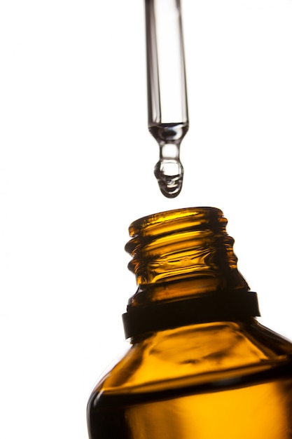 Gota de aceite que gotea de la pipeta en una botella de aceite esencial