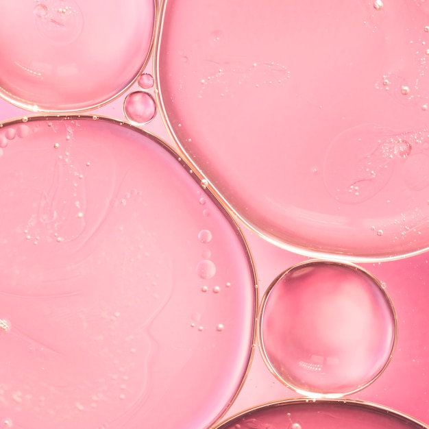 Gotas de aceite translúcido en líquido sobre fondo liso rosa borrosa