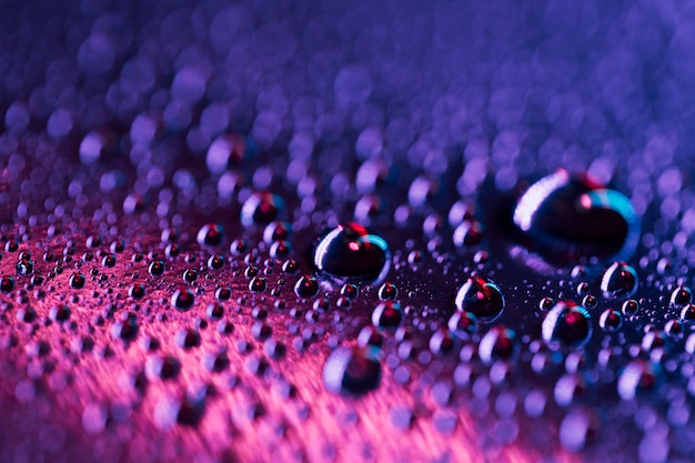 Gotas de agua sobre una superficie de vidrio brillante azul y rosa
