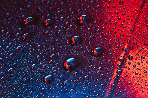 Gotas de agua sobre el vidrio con fondo texturizado rojo y azul