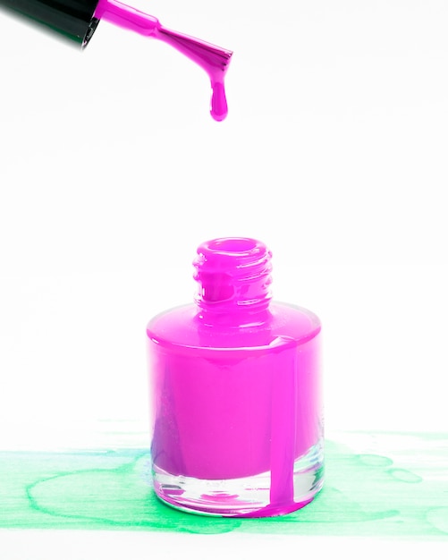 Goteo del esmalte de uñas rosado del cepillo en botella en fondo