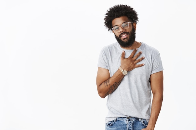 Gracias compañero, aprecio el esfuerzo Retrato de un chico afroamericano agradecido, fresco y elegante, con la palma en el corazón y sonriendo, agradecido, dando gracias a los amigos por la ayuda sobre el fondo gris