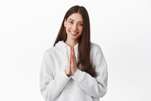 Gracias namaste Una joven sonriente se ve cariñosa y complacida tomándose de la mano en un gesto de rogar y rezar agradecida por la ayuda de pie sobre un fondo blanco