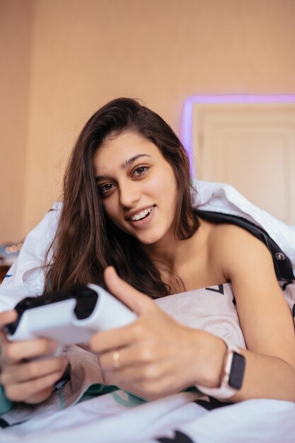 Graciosa acostada en la cama y jugando videojuegos, sosteniendo el controlador