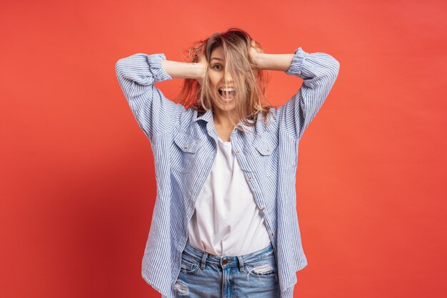 Graciosa, linda chica divirtiéndose mientras juega con el pelo aislado en una pared roja