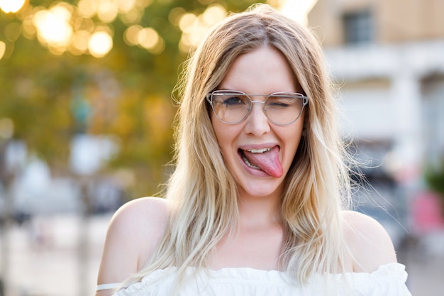 Graciosa mujer rubia mostrando lengua larga y guiñando un ojo