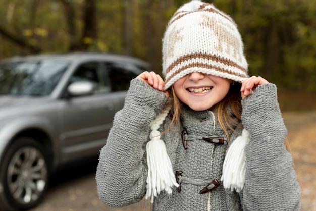 Foto gratuita graciosa niña que cubre su rostro con sombrero de invierno