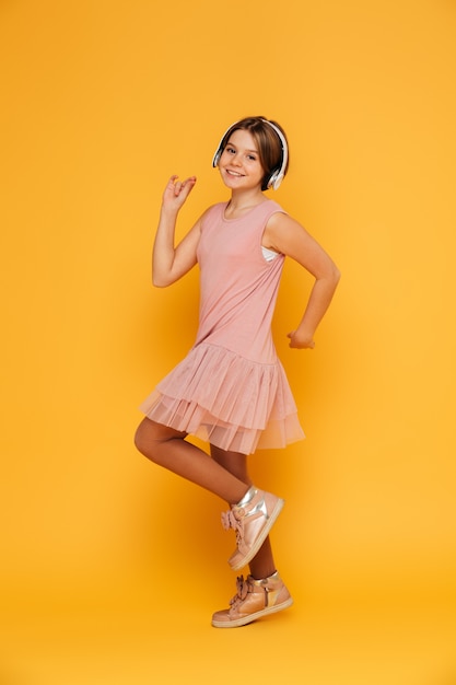 Graciosa niña sonriente en auriculares bailando aislado sobre amarillo