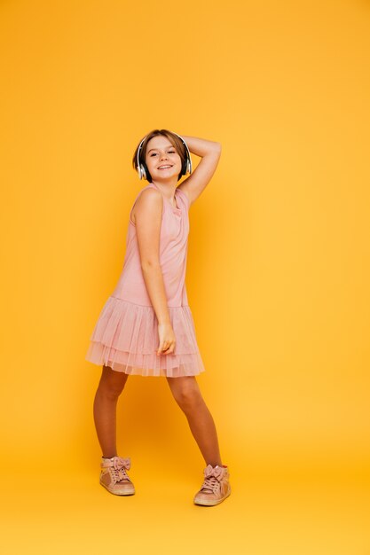 Graciosa niña sonriente en auriculares posando aislado sobre amarillo