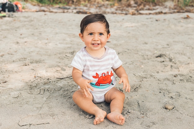 Gracioso bebé sentado en la playa de arena