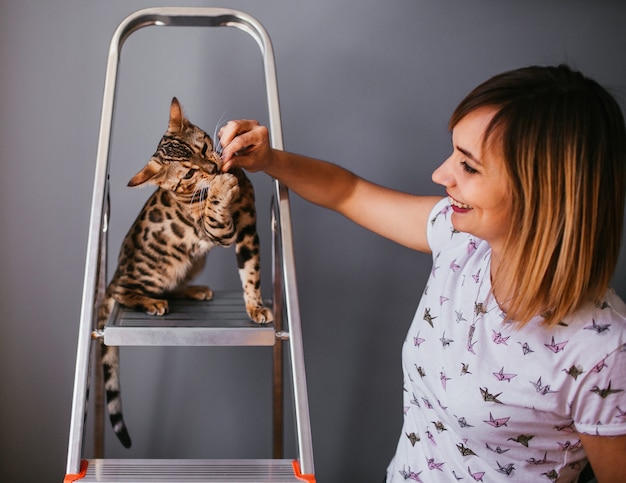 Gracioso gato de Bengala juega en la escalera de acero con una mujer