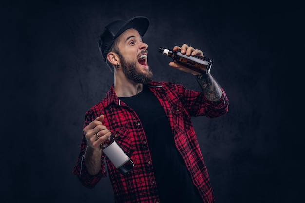 Gracioso hipster borracho barbudo sostiene una botella de cerveza.