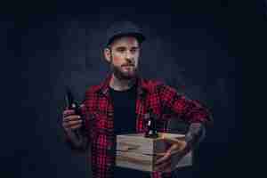 Foto gratuita gracioso hipster borracho barbudo sostiene una caja de madera con botellas de cerveza, de pie en el estudio.