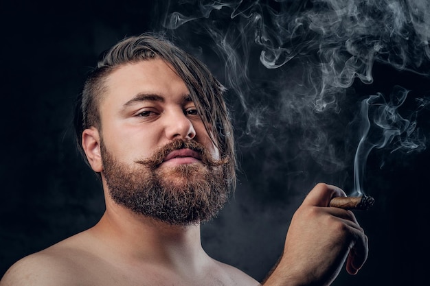 Foto gratuita gracioso hombre barbudo sin camisa fumando un cigarro sobre fondo gris.