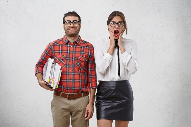 Gracioso hombre barbudo con grandes gafas con lentes gruesos mantiene muchos libros para impartir lecciones para una mujer joven y bonita