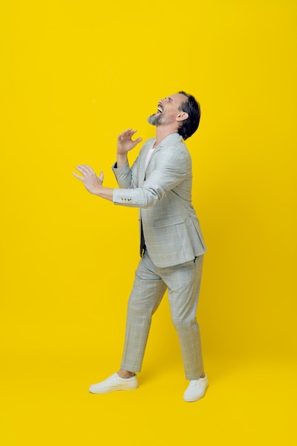 Gracioso hombre de negocios de mediana edad pretende tocar el saxofón riendo con los ojos cerrados aislado sobre fondo amarillo Guapo hombre de negocios maduro en traje blanco Concepto de negocio Copiar espacio