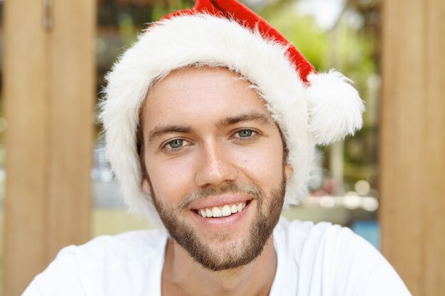 Gracioso joven de sombrero rojo con pelaje blanco sonriendo felizmente, disfrutando de unas vacaciones en un país con clima cálido.