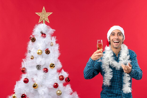 Gracioso joven con sombrero de santa claus en una camisa azul a rayas sosteniendo una copa de vino