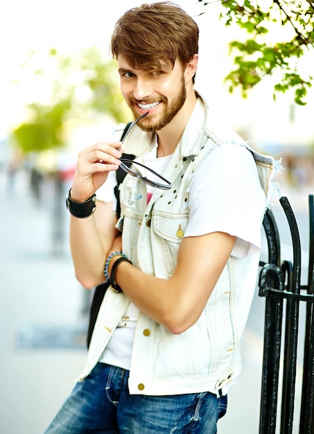 Foto gratuita gracioso sonriente hipster hombre guapo en elegante ropa de verano en la calle con gafas de sol