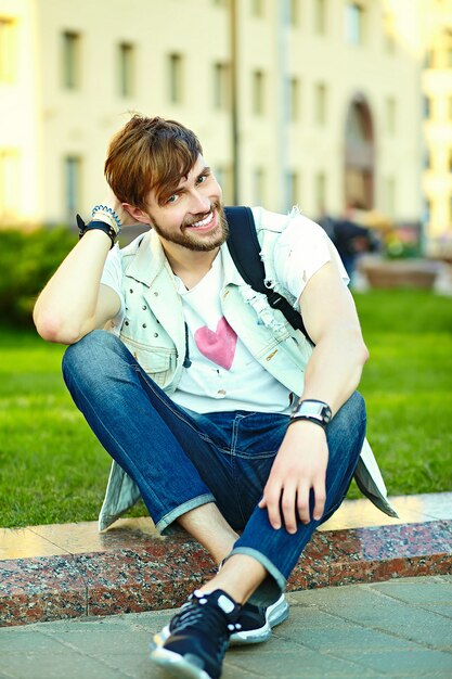 Gracioso sonriente hipster hombre guapo en elegante ropa de verano en la calle con gafas de sol