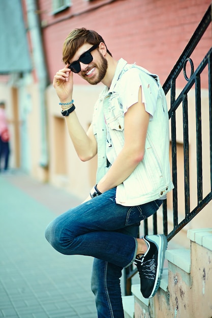 Gracioso sonriente hipster hombre guapo en elegante ropa de verano en la calle con gafas de sol