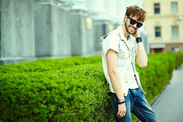 Gracioso sonriente hipster hombre guapo en elegante ropa de verano en la calle con gafas de sol