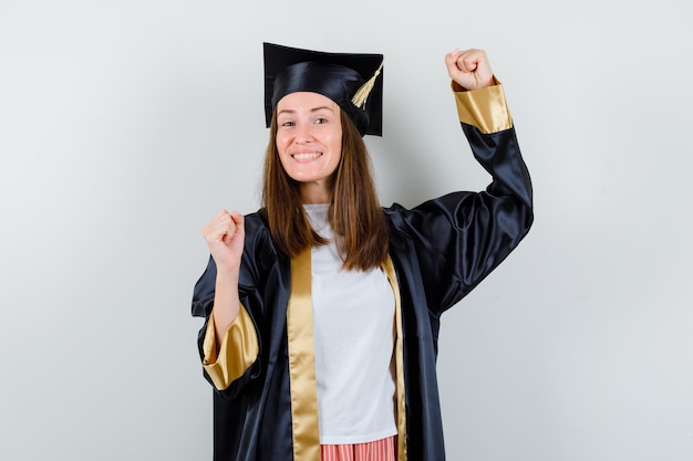 Graduada femenina mostrando gesto ganador en traje académico y mirando feliz. vista frontal.