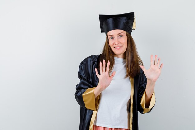 Graduada femenina mostrando gesto de parada en uniforme, ropa casual y mirando confiado, vista frontal.