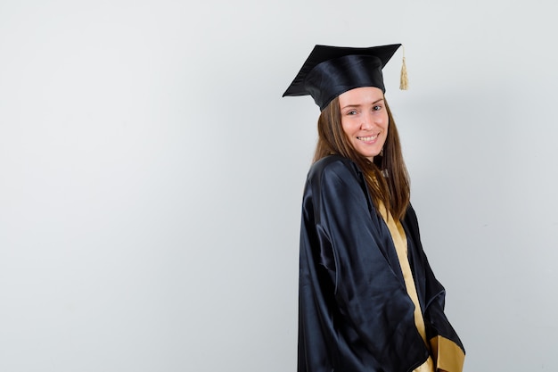 Graduada femenina posando mientras está de pie en traje académico y se ve feliz. .